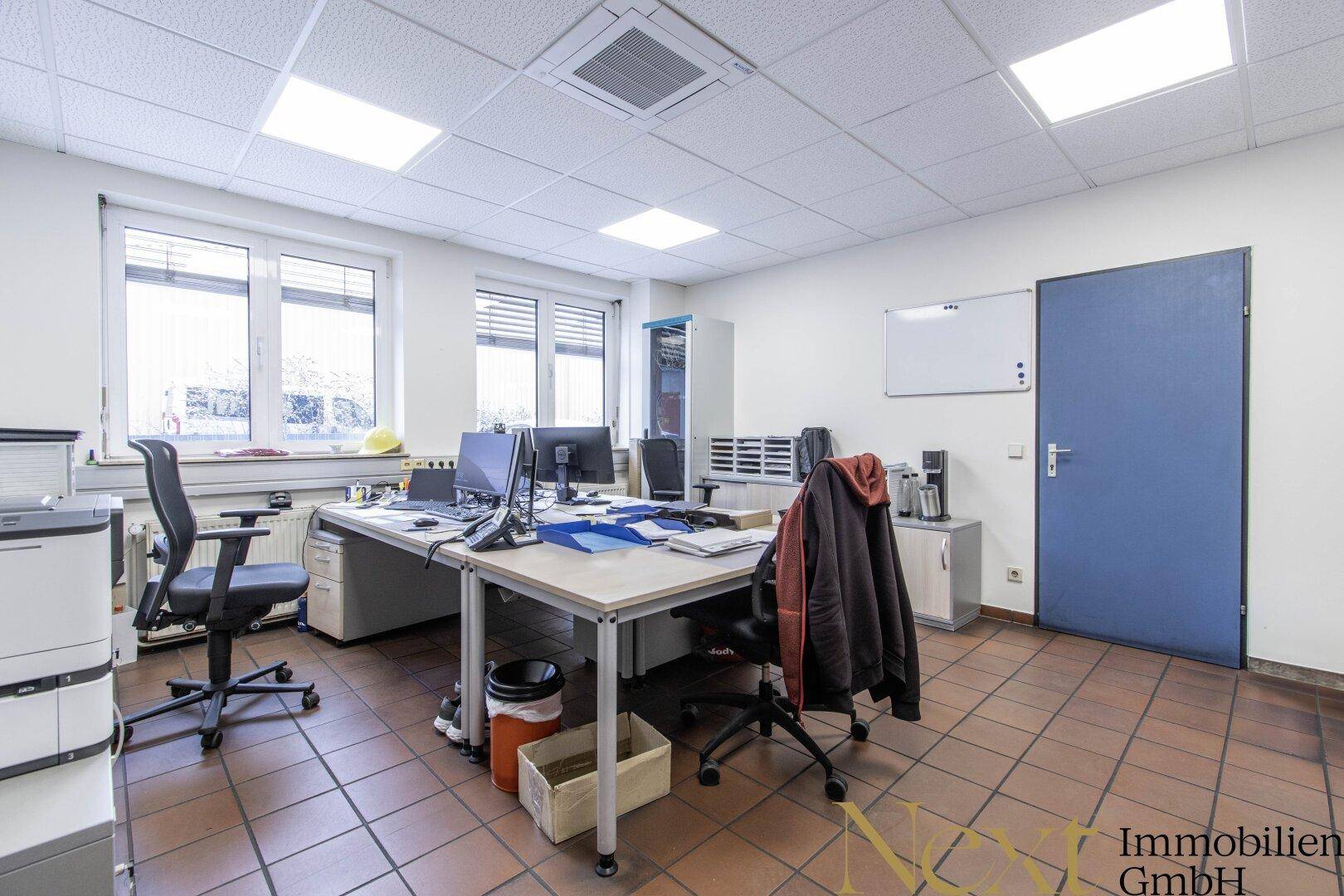 Büro mit mehreren Arbeitsplätzen, Computern, Bürostühlen und Terrakotta-Bodenfliesen.