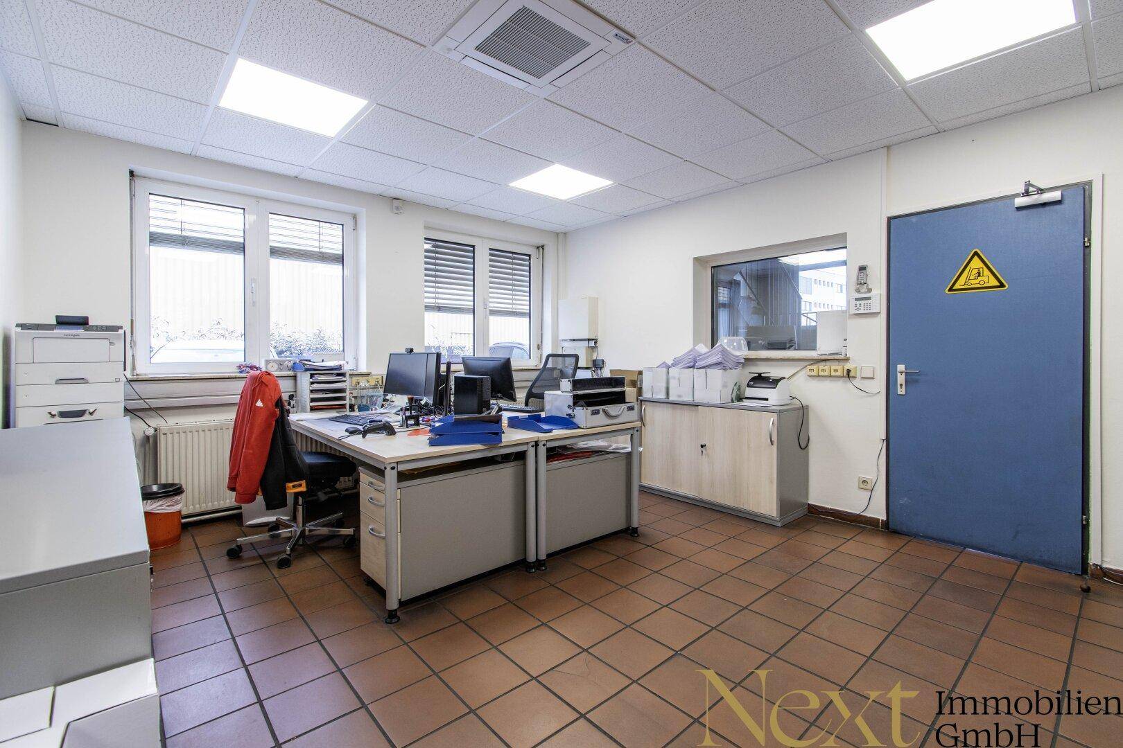 Helles Büro mit mehreren Schreibtischen, Büromöbeln und einem Fenster mit Blick nach draußen.