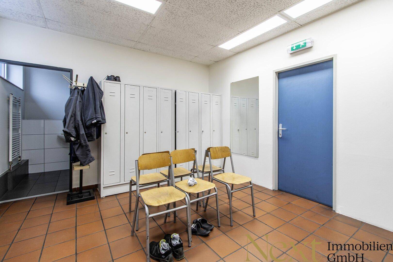Umkleideraum mit Spinden, Stühlen und Zugang zu den Duschbereichen, ausgestattet mit Terrakotta-Bodenfliesen.