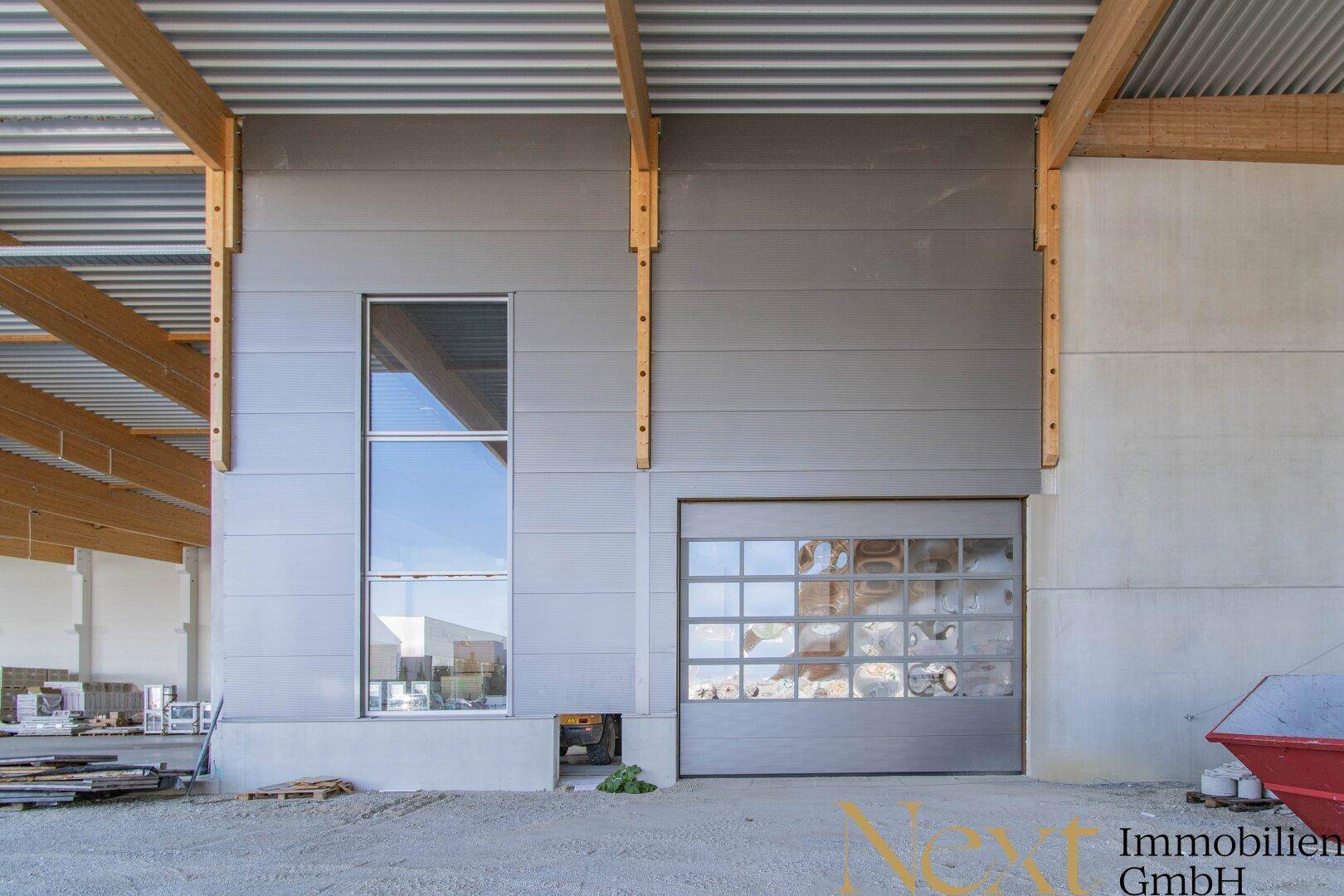 Moderne Industriefassade mit großem Fenster und Rolltor, unter einem Holzdachüberstand.