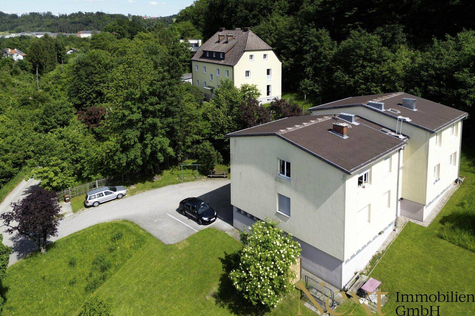 Übersicht der Wohngebäude von oben, umgeben von viel Grün und mit Stellplätzen.