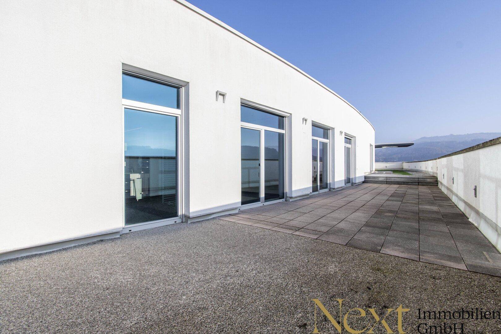 Weitläufige Dachterrasse mit Fliesenboden und weißer Fassade, bietet viel Platz im Freien.