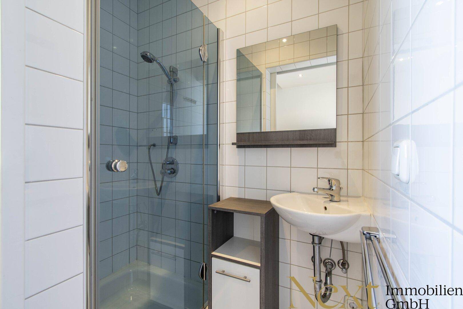Modernes Badezimmer mit Duschkabine, Waschbecken und weißen Fliesen an den Wänden.