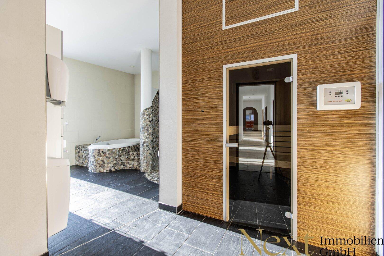 Geräumiges Badezimmer mit Sauna-Zugang, dunklem Fliesenboden und dekorativen Wänden.