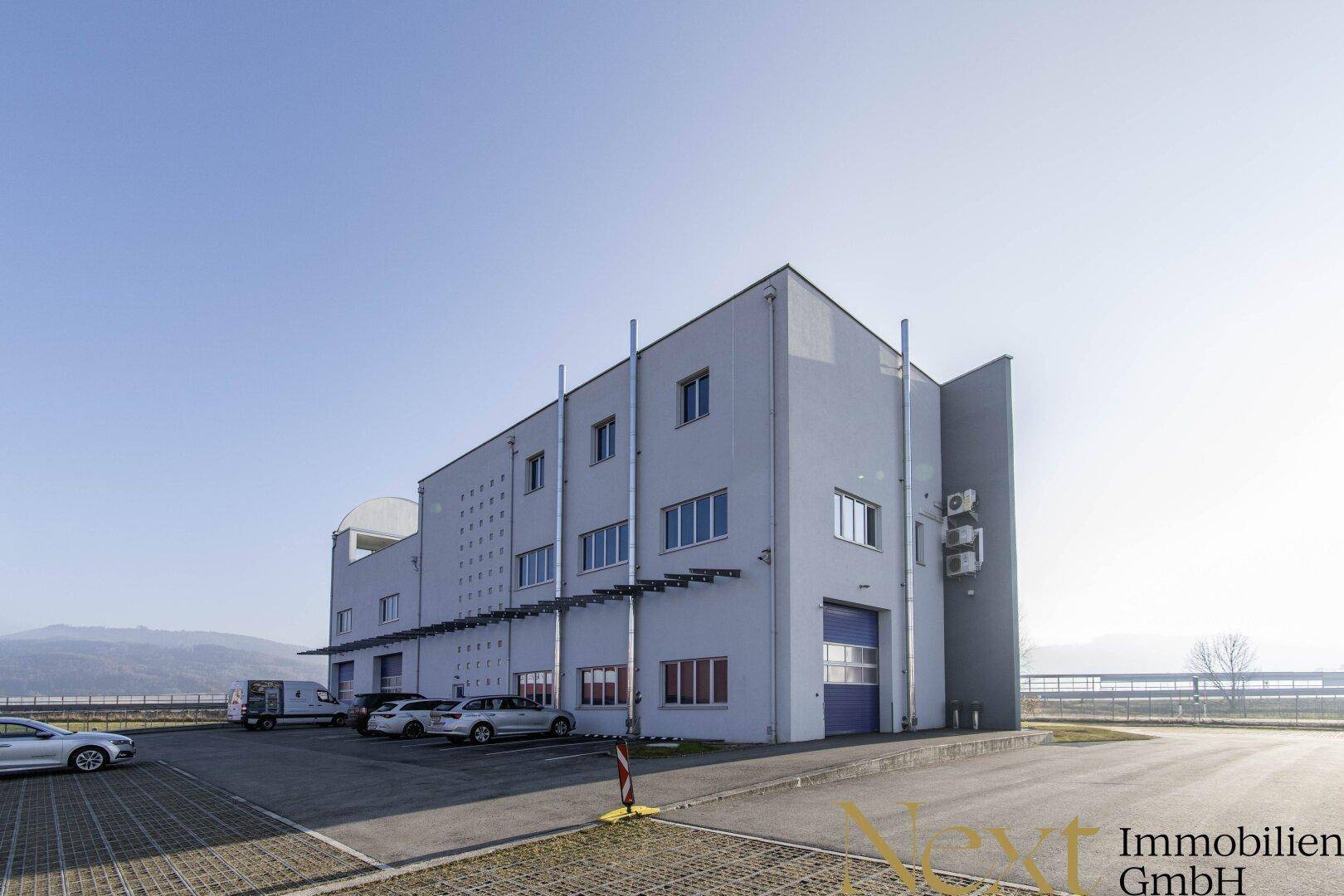 Industrielles Gebäude mit Parkplätzen, Laderampen und moderner Architektur in ländlicher Umgebung.