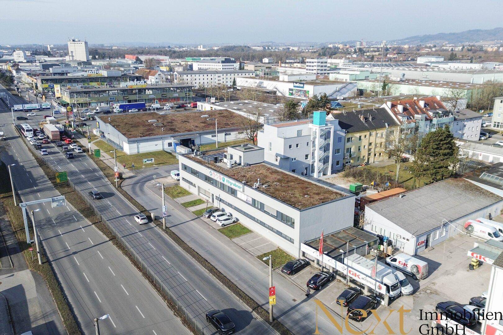 Weitläufige Luftaufnahme eines Gewerbegebiets mit dem modernen Gebäude, belebten Straßen und weiteren Gebäuden im Hintergrund.