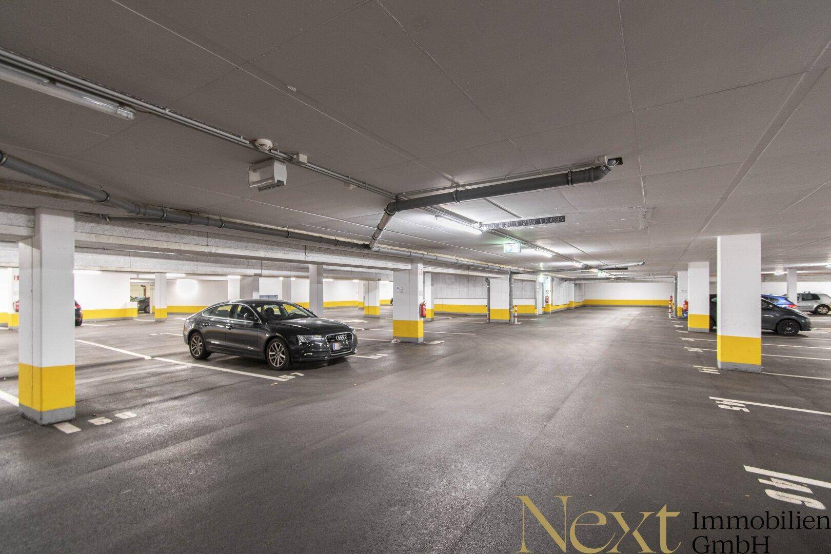 Geräumige Tiefgarage mit zahlreichen Stellplätzen, hell beleuchtet und mit robusten Betonpfeilern.