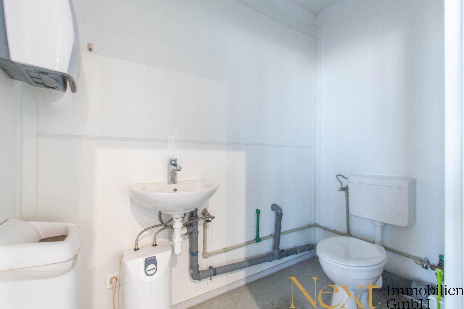 Einfache Toilette mit Waschbecken und sichtbaren Rohrleitungen, in einem funktionalen Stil gehalten.