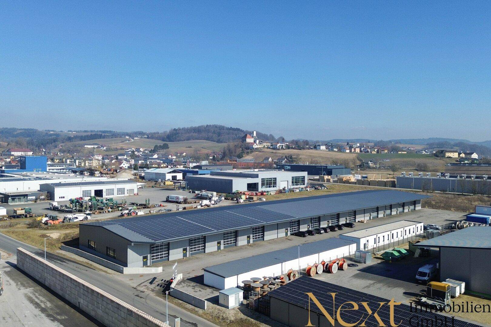 Luftaufnahme eines modernen Gewerbeparks mit mehreren Hallen und Photovoltaikanlagen auf den Dächern.
