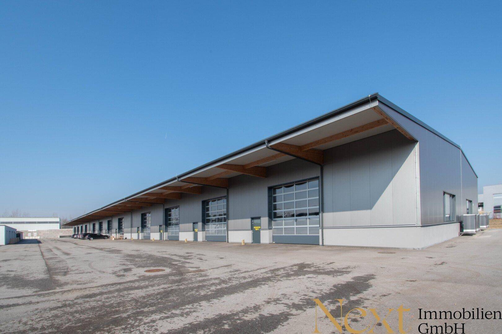 Moderne Gewerbehalle mit langer Fassade, großen Rolltoren und überdachtem Eingangsbereich, ideal für Logistik.