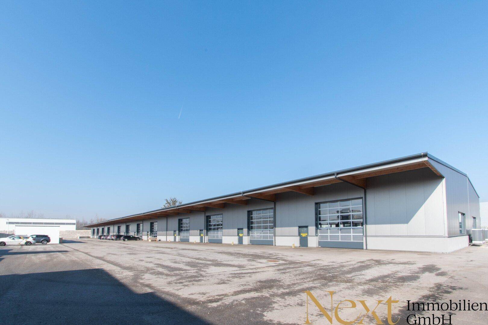 Moderne Gewerbehalle mit mehreren Rolltoren und einem großen asphaltierten Vorplatz unter klarem blauem Himmel.
