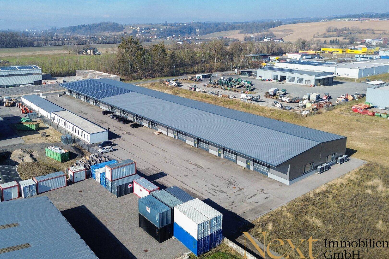 Luftaufnahme eines modernen Gewerbegebäudes mit Solaranlage auf dem Dach und weitläufigem Außengelände.