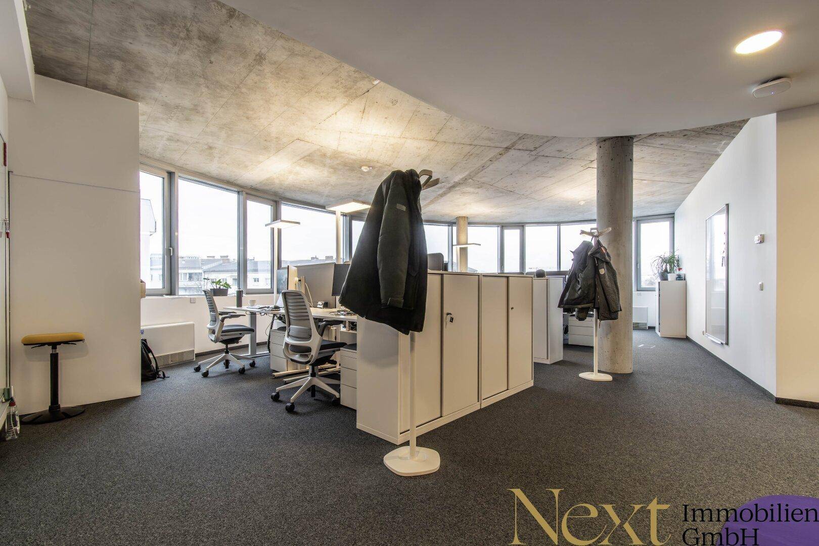 Ein geräumiger Bürobereich mit mehreren Arbeitsplätzen, großen Fenstern und einem modernen Design.