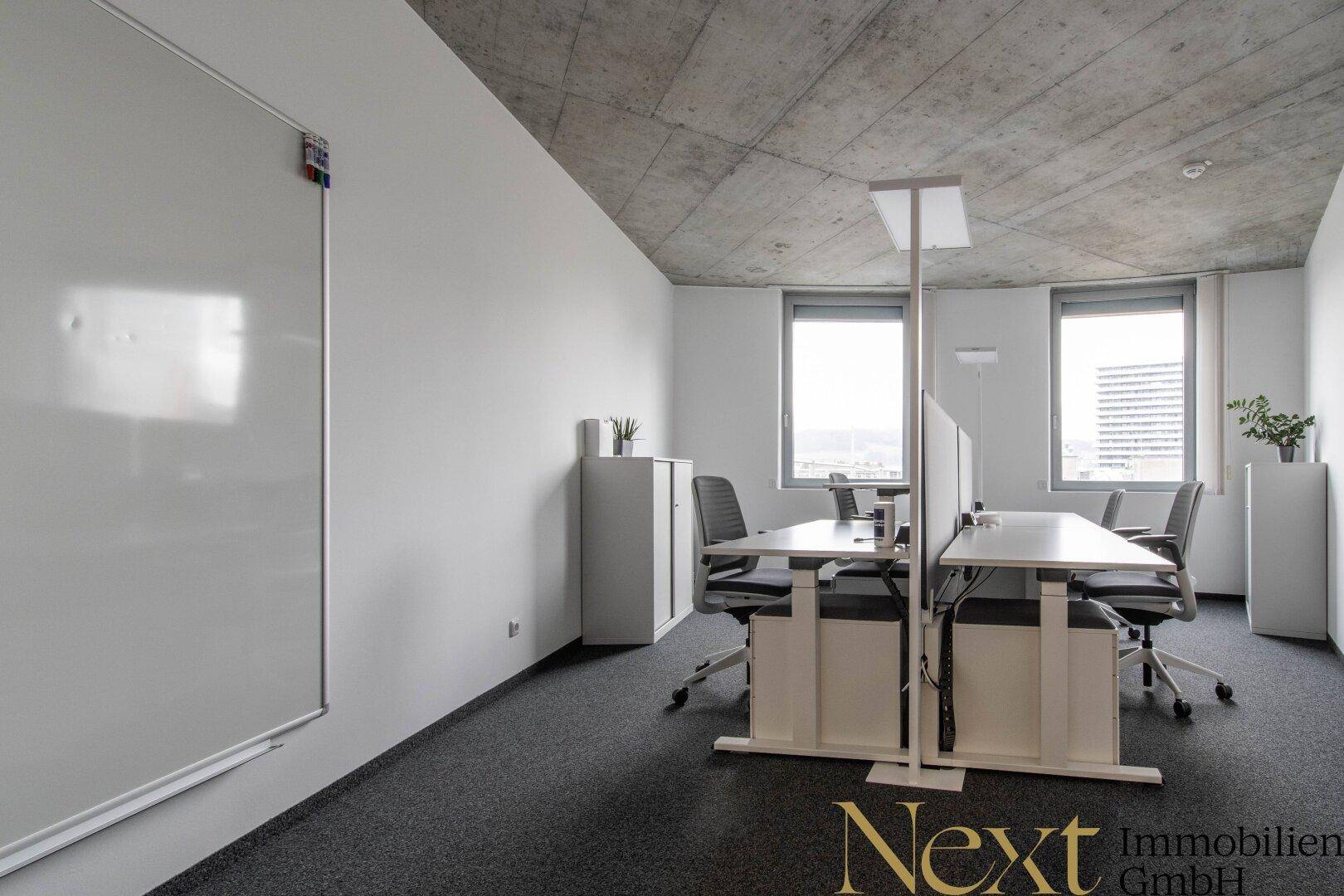 Ein heller Bürobereich mit weißen Wänden, Teppichboden und einer großen Whiteboard-Wand für Präsentationen.