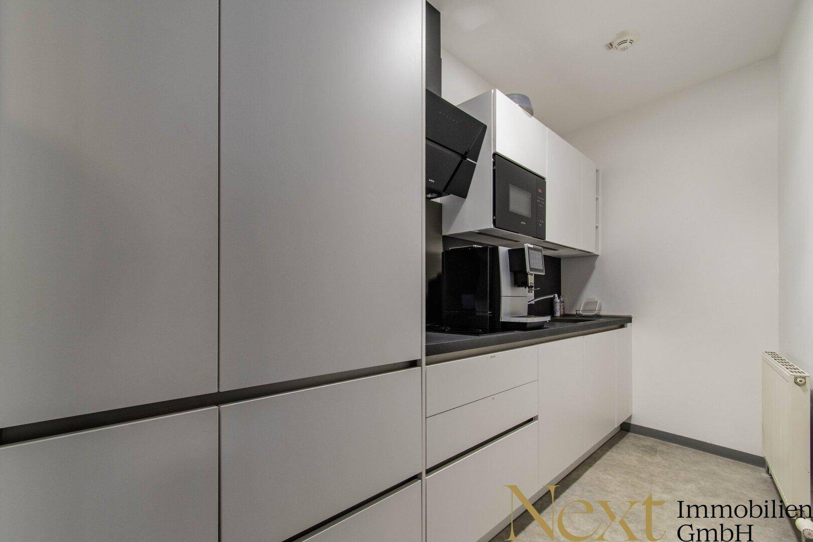 Eine moderne, minimalistische Küche mit weißen Schränken, dunkler Arbeitsplatte und integrierten Geräten.