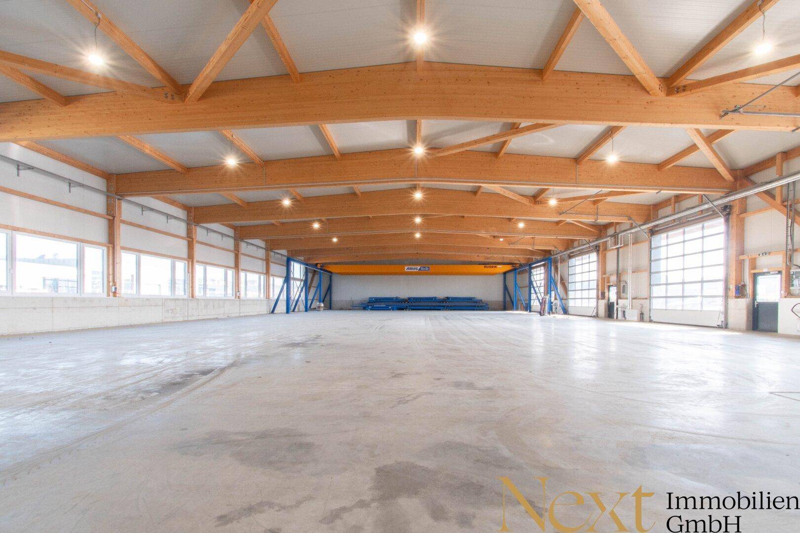 Geräumige Lagerhalle mit hoher Holzkonstruktion und viel Tageslicht durch zahlreiche Fenster.
