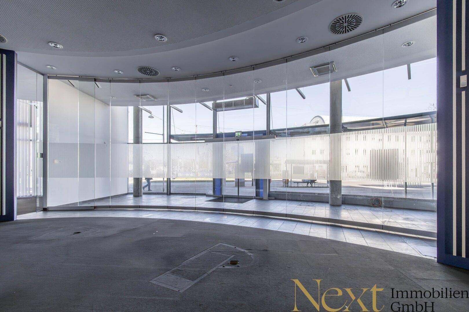 Heller Gewerberaum mit großer Glasfront, die viel Tageslicht hereinlässt und einen Blick nach draußen bietet.