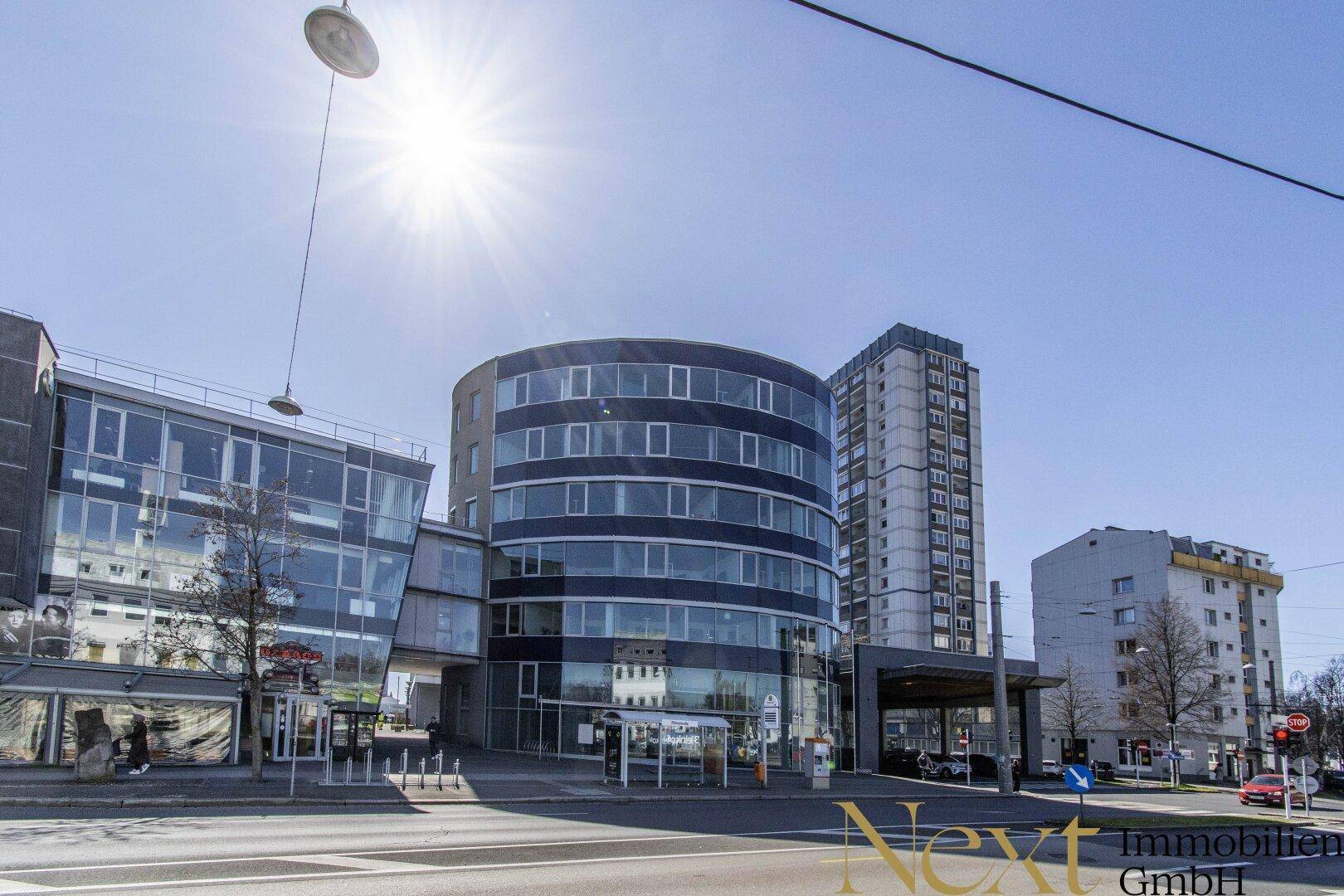 Beeindruckendes modernes Gebäude mit runder Glasfassade an einer belebten Straße unter strahlendem Sonnenschein.