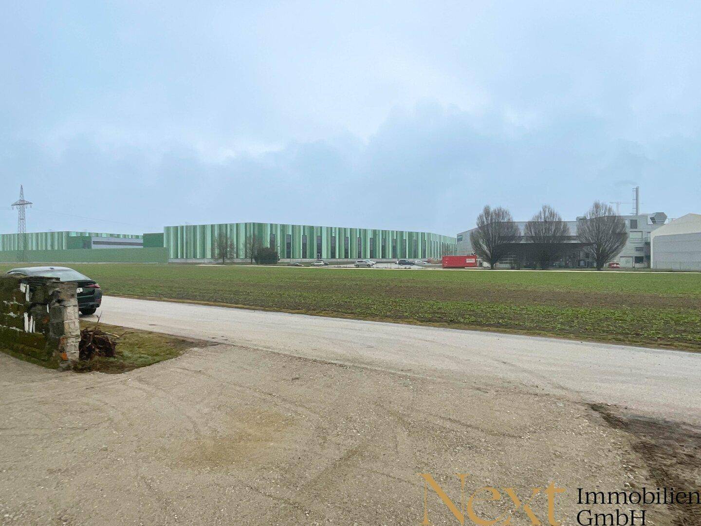 Weitläufige Felder mit Blick auf ein modernes Industriegebäude in der Ferne.