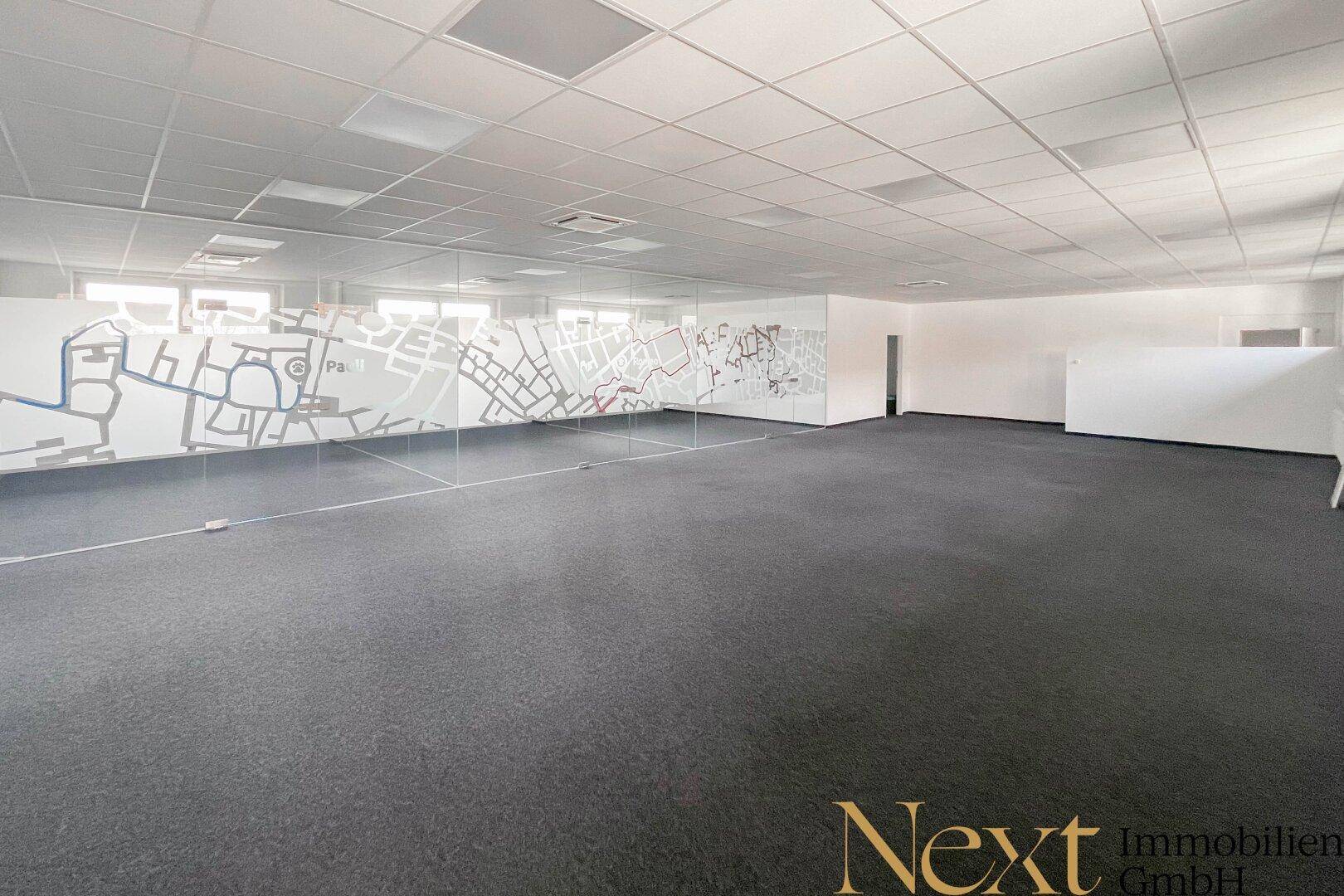 Großes Büro mit Teppichboden und modernen Glaswänden, die eine offene Raumgestaltung ermöglichen und viel Licht bieten.