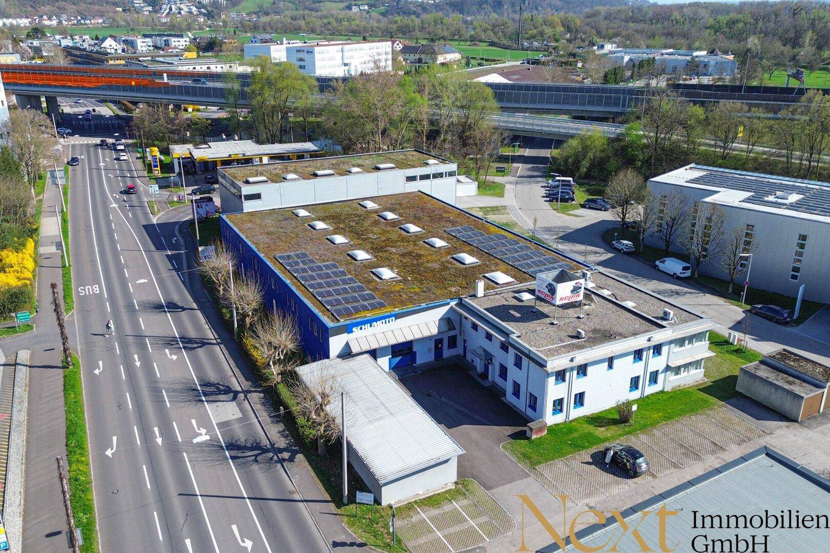 Weitläufige Luftaufnahme eines Gewerbegebiets mit Hauptstraße, Parkplätzen und Gebäuden mit Solaranlagen auf den Dächern.