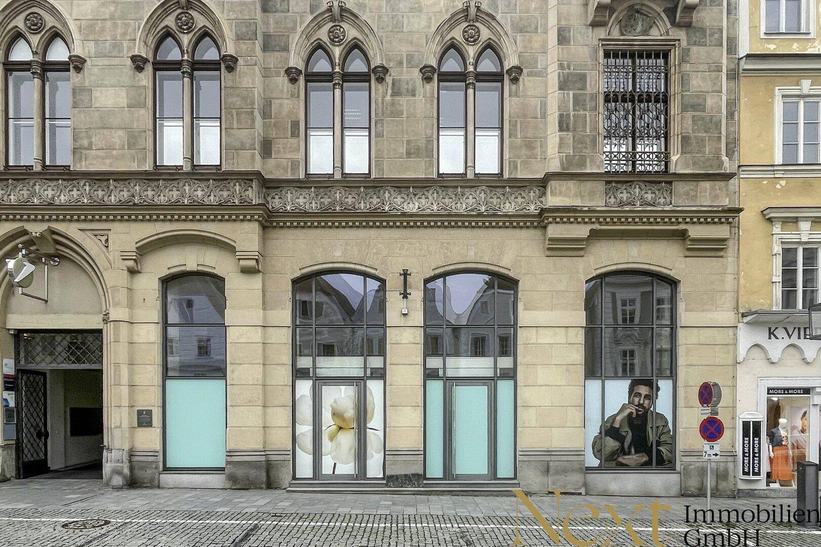 Detailansicht der historischen Fassade im Erdgeschoss mit großen Schaufenstern und Eingangstüren an einer belebten Straße.