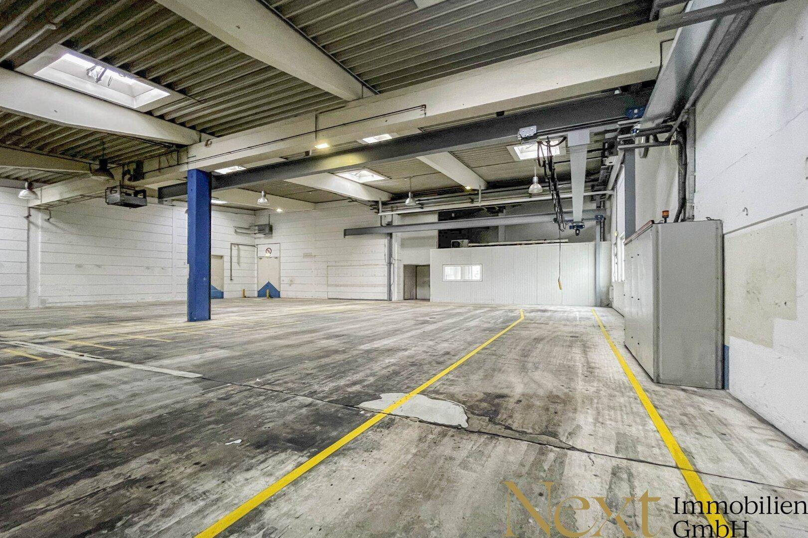 Geräumige Lagerhalle mit Betonboden, blauer Säule und industrieller Deckenkonstruktion.
