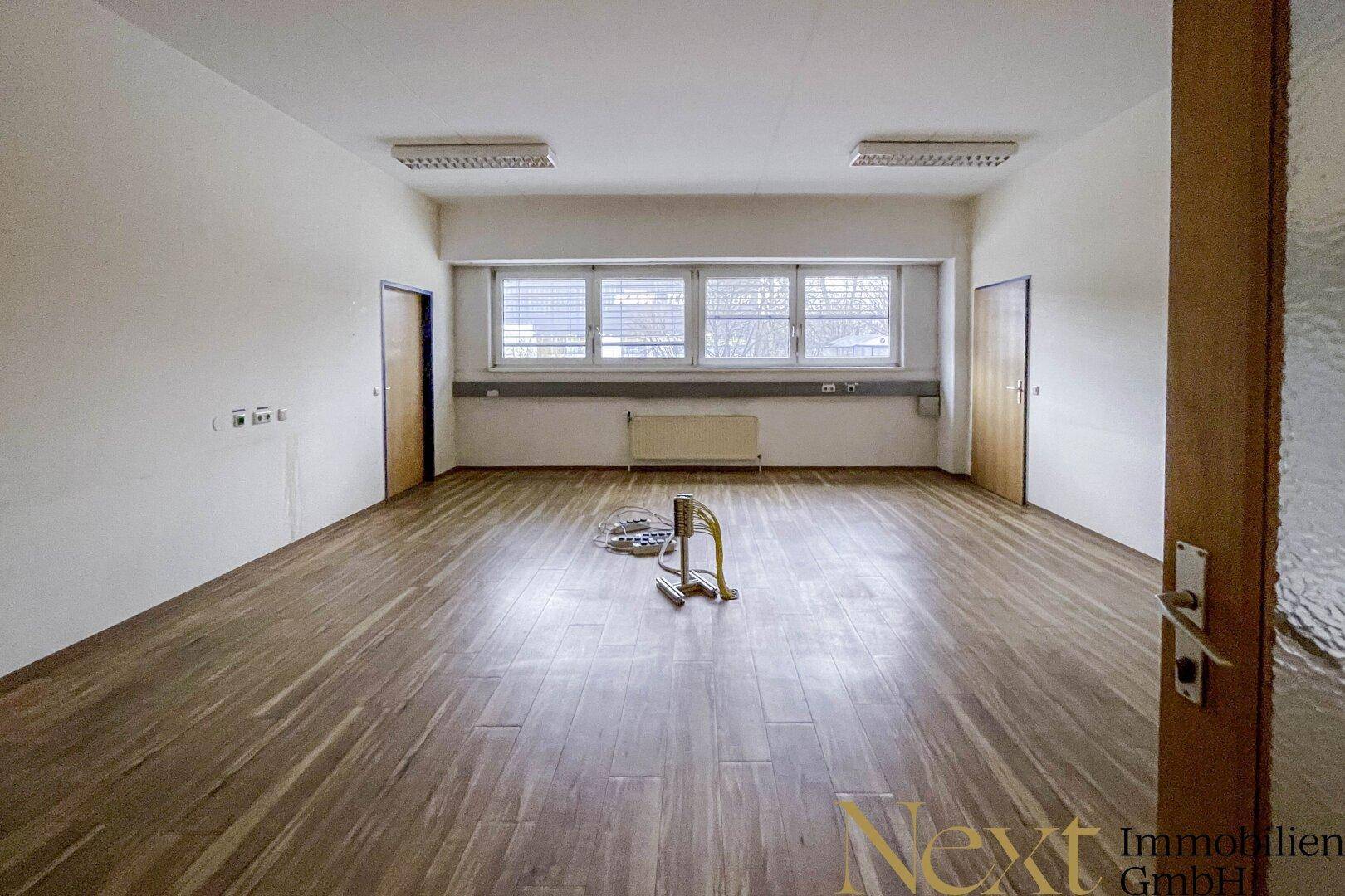 Leeres Büro mit Holzfußboden und mehreren Türen, bereit zur individuellen Gestaltung.