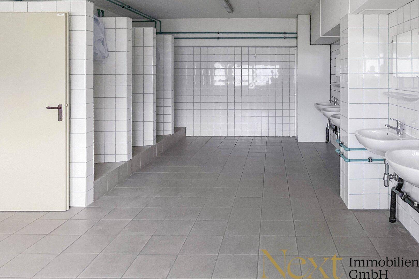 Sanitärbereich mit mehreren Waschbecken und gefliesten Duschkabinen, funktional und sauber.