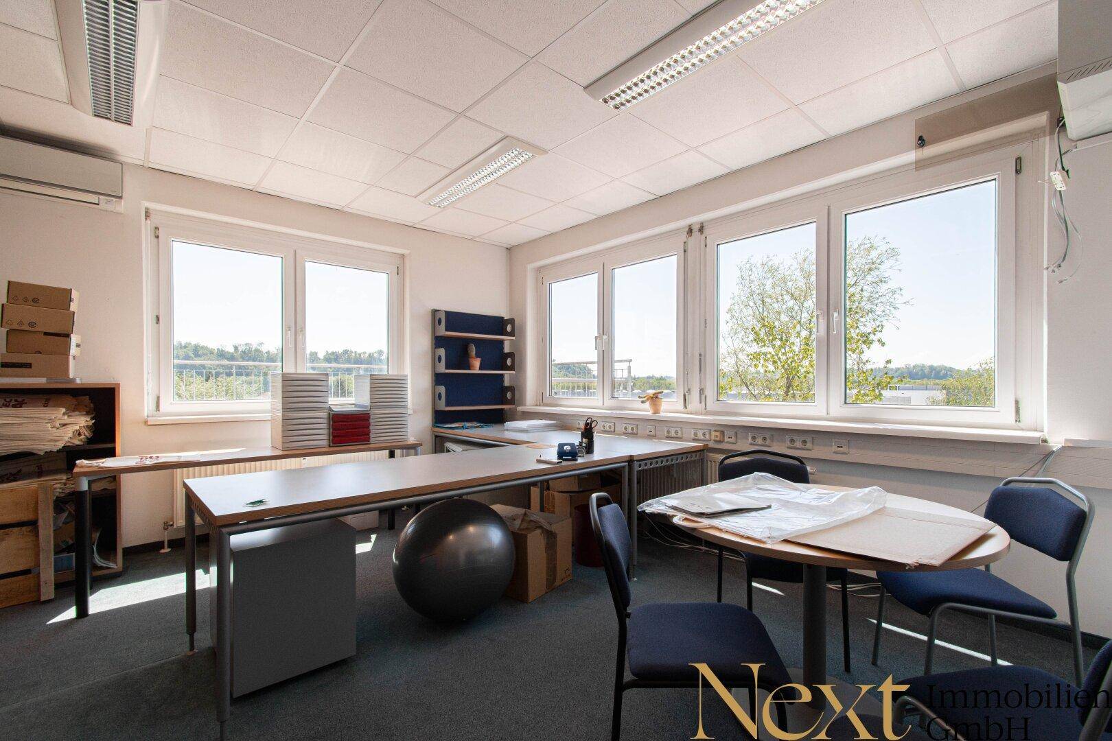 Helles Büro mit mehreren Arbeitsplätzen, großen Fenstern und Blick ins Grüne sowie Klimaanlage.