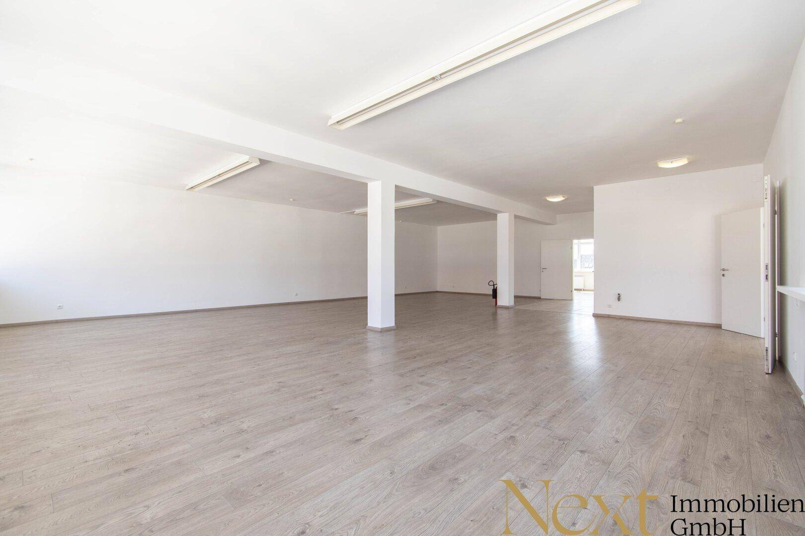Großer, heller Büroraum mit Säulen und modernem Laminatboden, ideal für offene Arbeitsbereiche.
