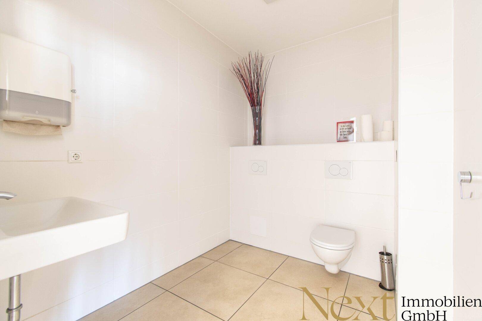 Saubere und helle Toilette mit Wand-WC, Waschbecken und Fliesenboden in neutralen Farben.