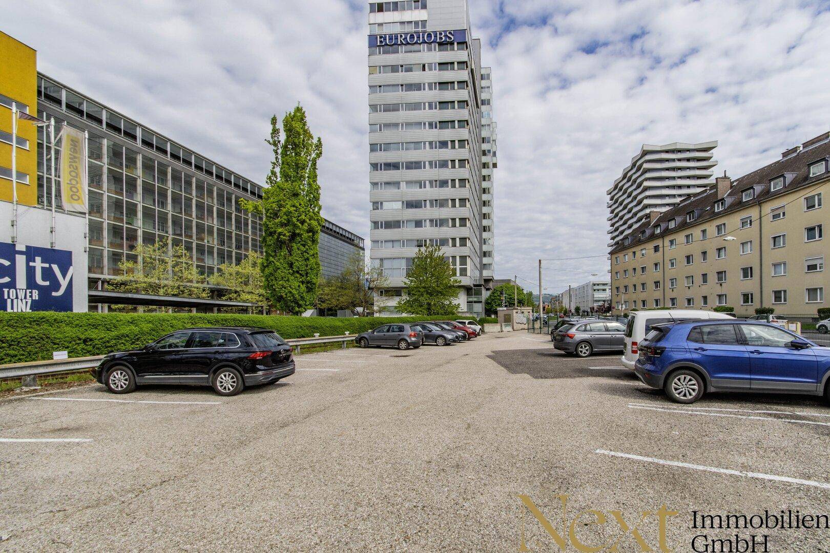 Außenansicht eines Parkplatzes umgeben von modernen Bürogebäuden in einer städtischen Umgebung.