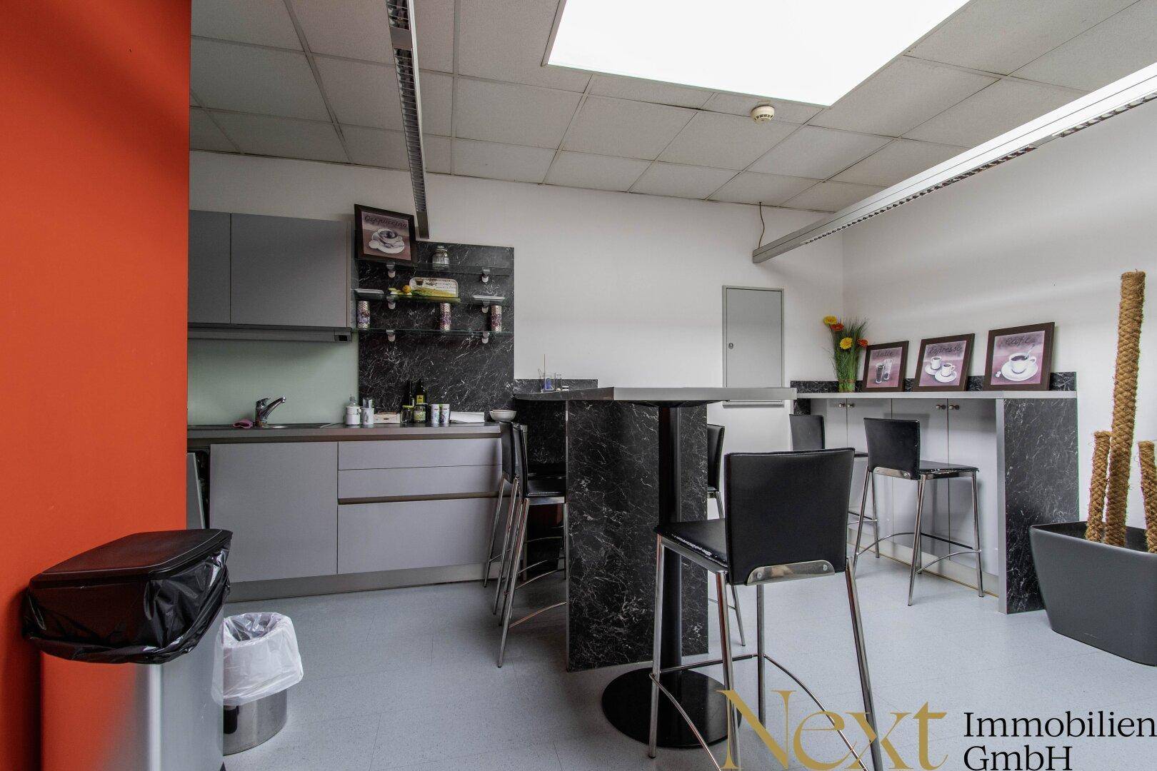 Moderne Büroküche mit dunklen Schränken, Bartischen und Hockern, ideal für Pausenbereiche.