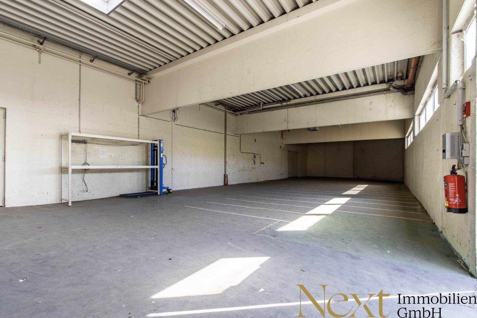 Große Lagerhalle mit Betonboden, hohen Decken und Regalen, ideal für industrielle Nutzung.