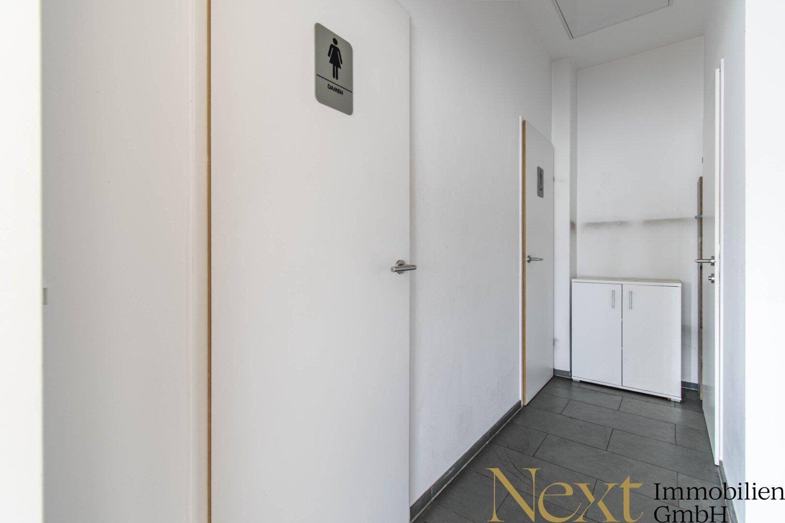 Eingangsbereich zu den Toiletten mit weißen Türen und dunklen Fliesen, sauber und funktional.