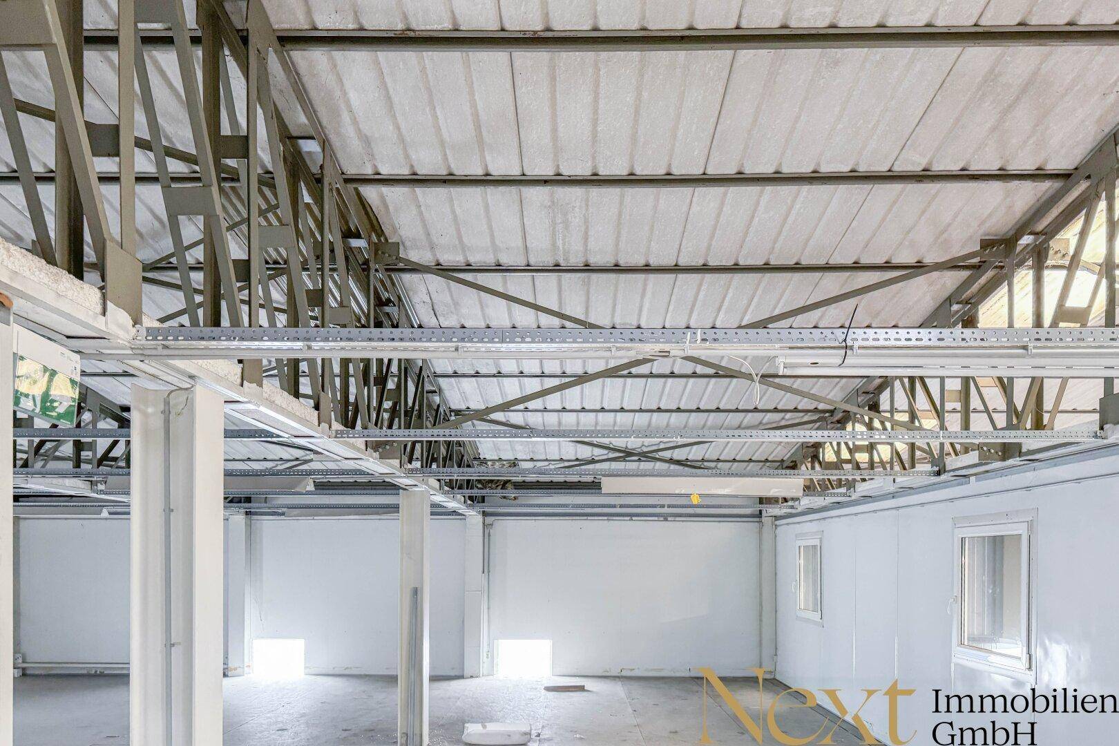 Leerer Raum mit sichtbarer Deckenkonstruktion und kleinen Fenstern, bereit für den Ausbau.