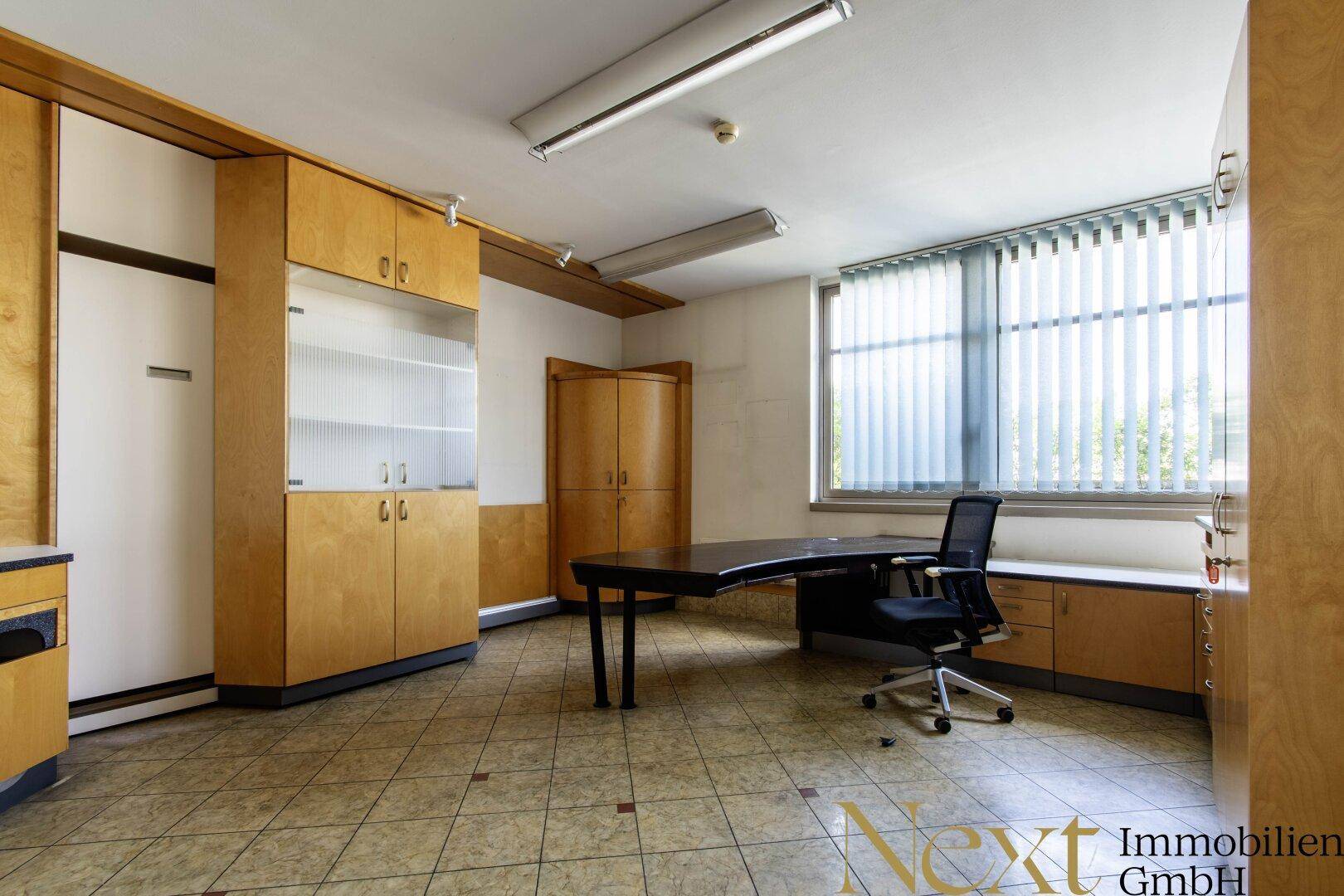 Funktionales Bürozimmer mit Schreibtisch, Bürostuhl, Einbauschränken und Fenster mit Jalousien.