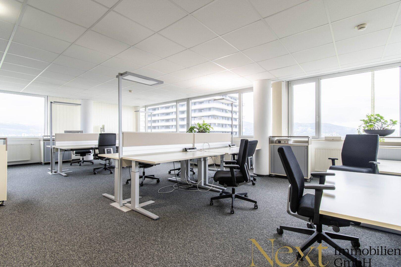 Helles Großraumbüro mit ergonomischen Arbeitsplätzen und weitem Ausblick durch die Fensterfront.