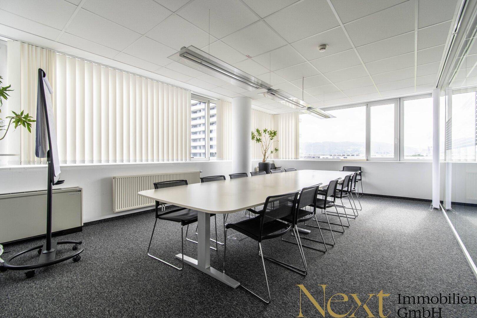Großer Konferenzraum mit langem Tisch, vielen Stühlen und weitem Blick durch die Fensterfront.