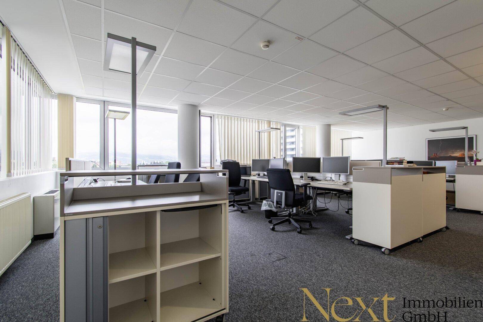 Offenes Büro mit mehreren Arbeitsplätzen, modernen Büromöbeln und viel Tageslicht.