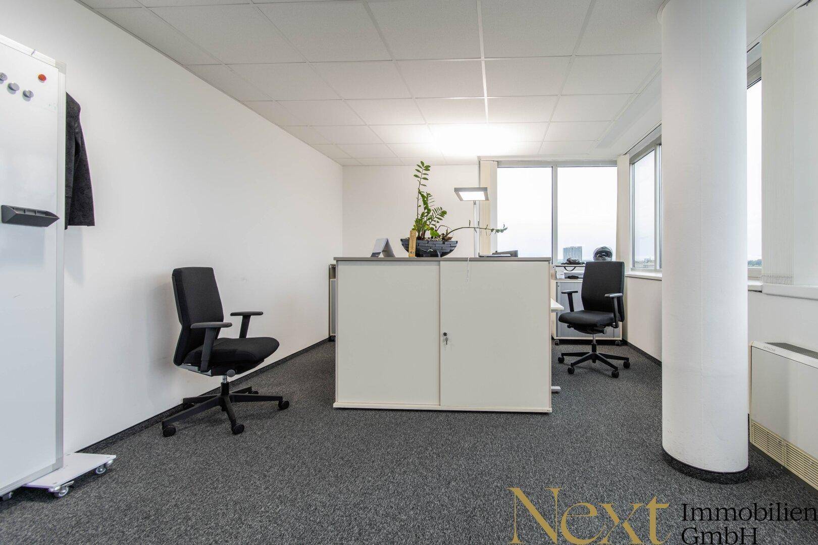 Einzelbüro oder kleiner Arbeitsbereich mit Schreibtisch, Bürostuhl und Fenster mit Ausblick.