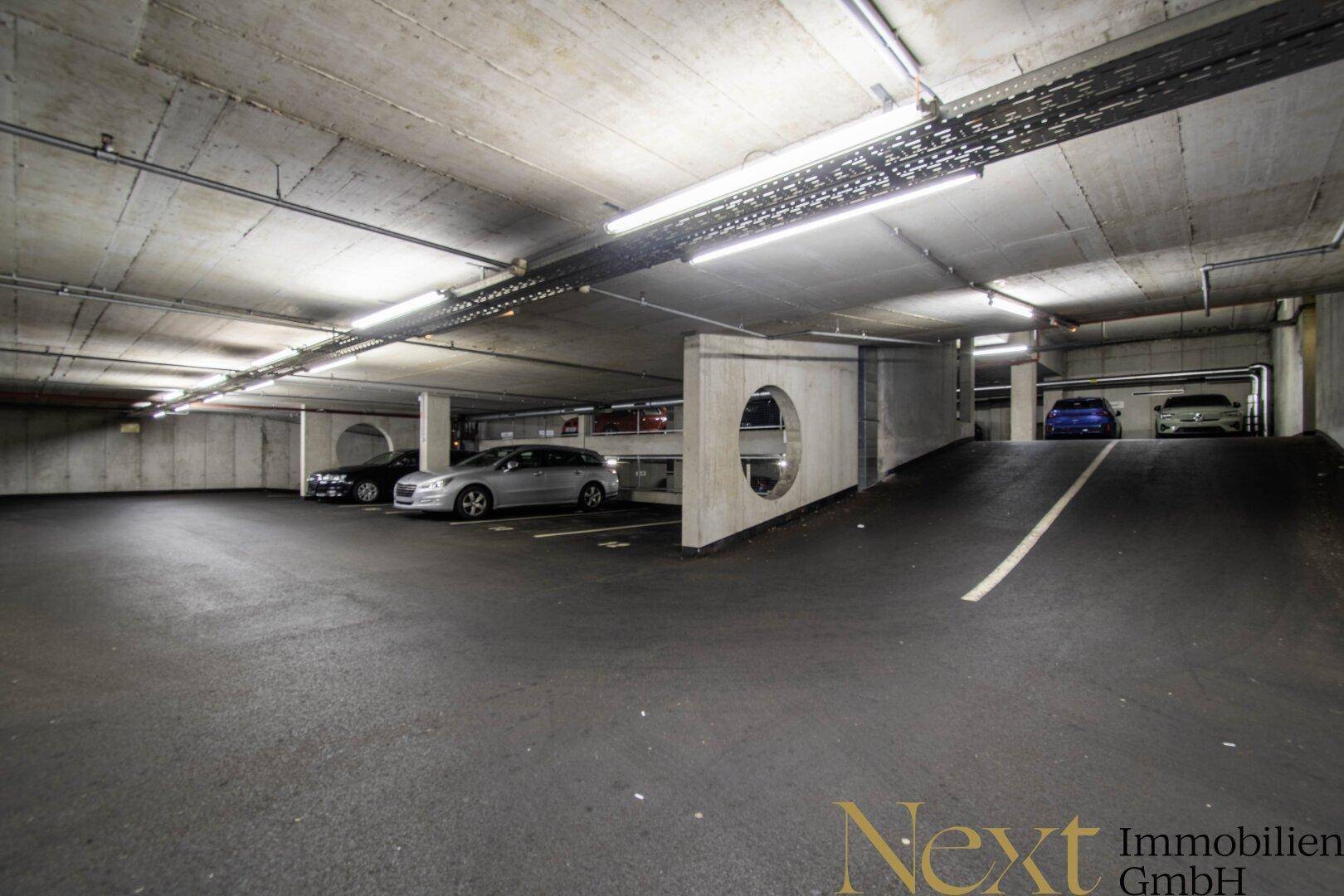 Tiefgarage mit mehreren Stellplätzen, Betonwänden und einer Rampe für die Zufahrt.