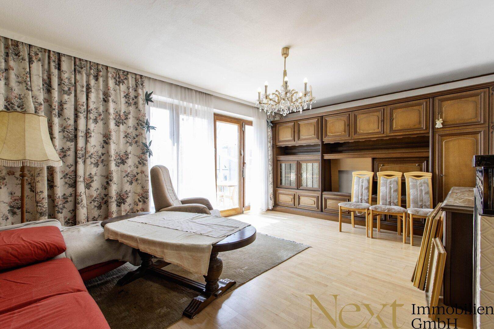 Geräumiges Wohnzimmer mit traditionellen Holzmöbeln, Parkettboden und Zugang zum Balkon.