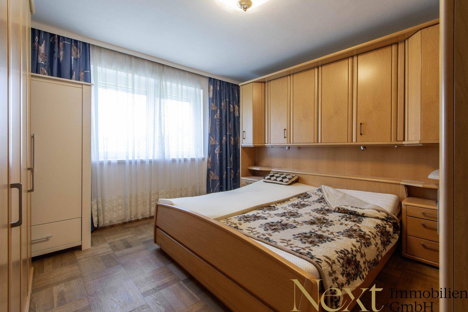 Schlafzimmer mit Einbauschränken, Doppelbett und Fenster mit Vorhängen.