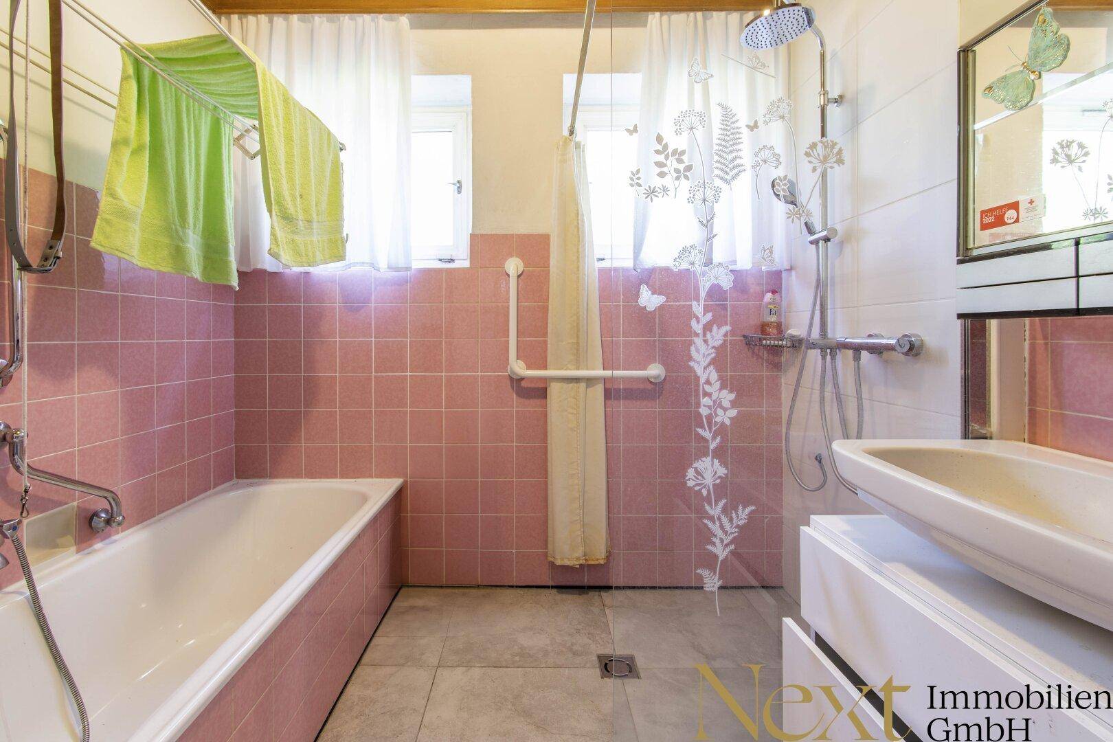 Badezimmer mit rosa Fliesen, Badewanne, Dusche und Fenster für Tageslicht.