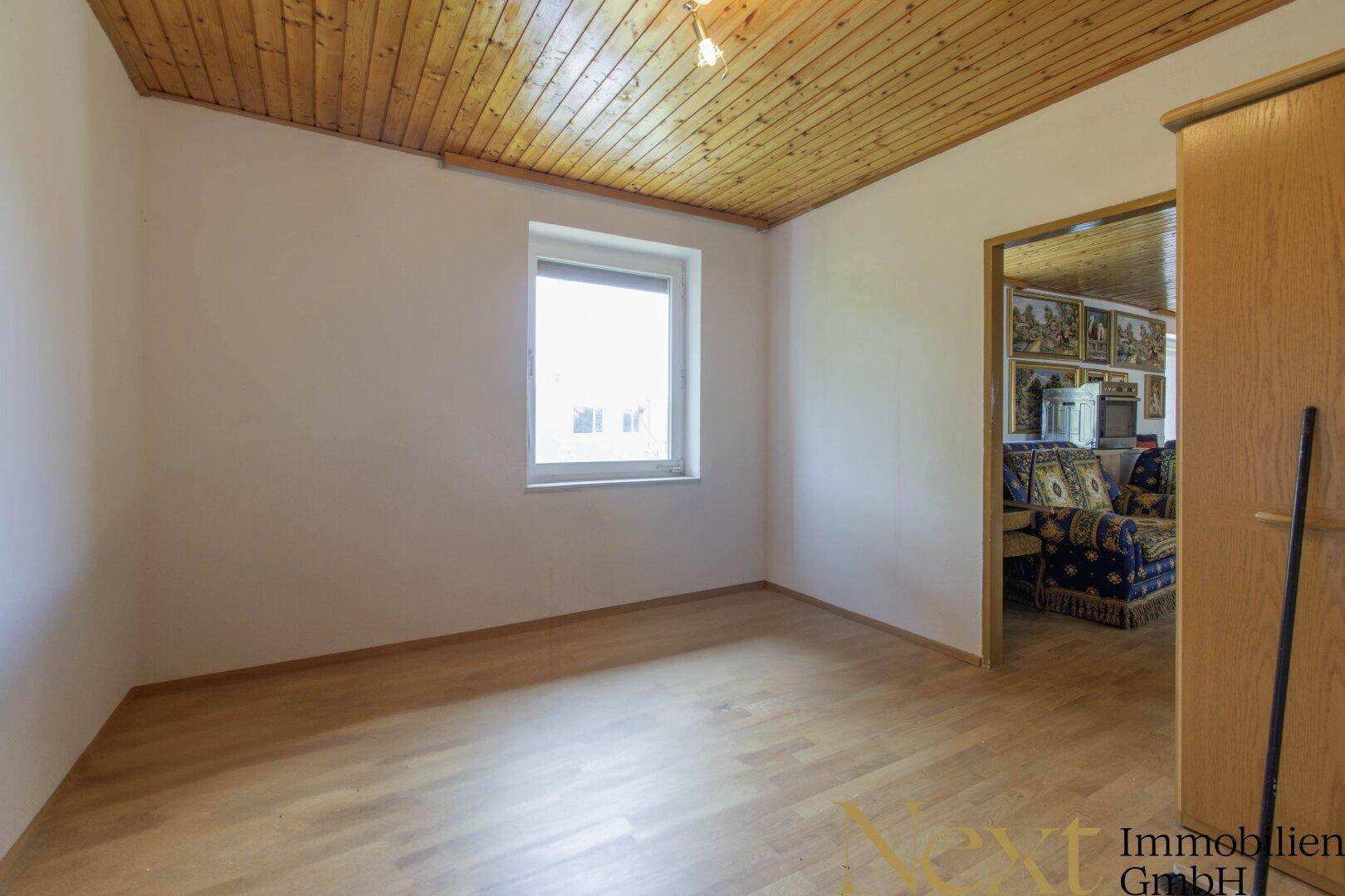 Schlafzimmer mit Holzboden und Fenster, das in einen weiteren Raum blickt.
