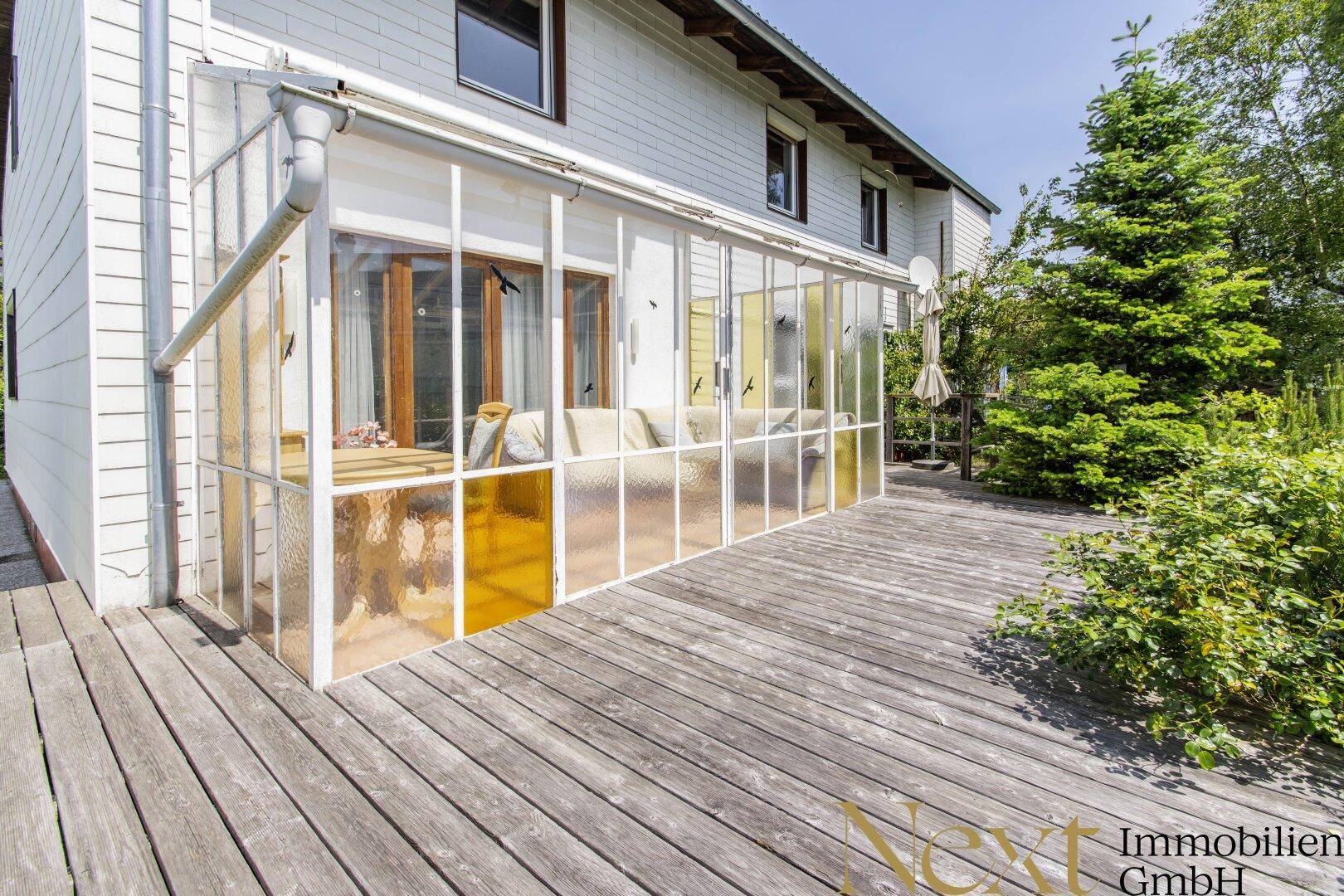 Verglaster Wintergarten auf einer Holzterrasse mit Sitzgelegenheiten.