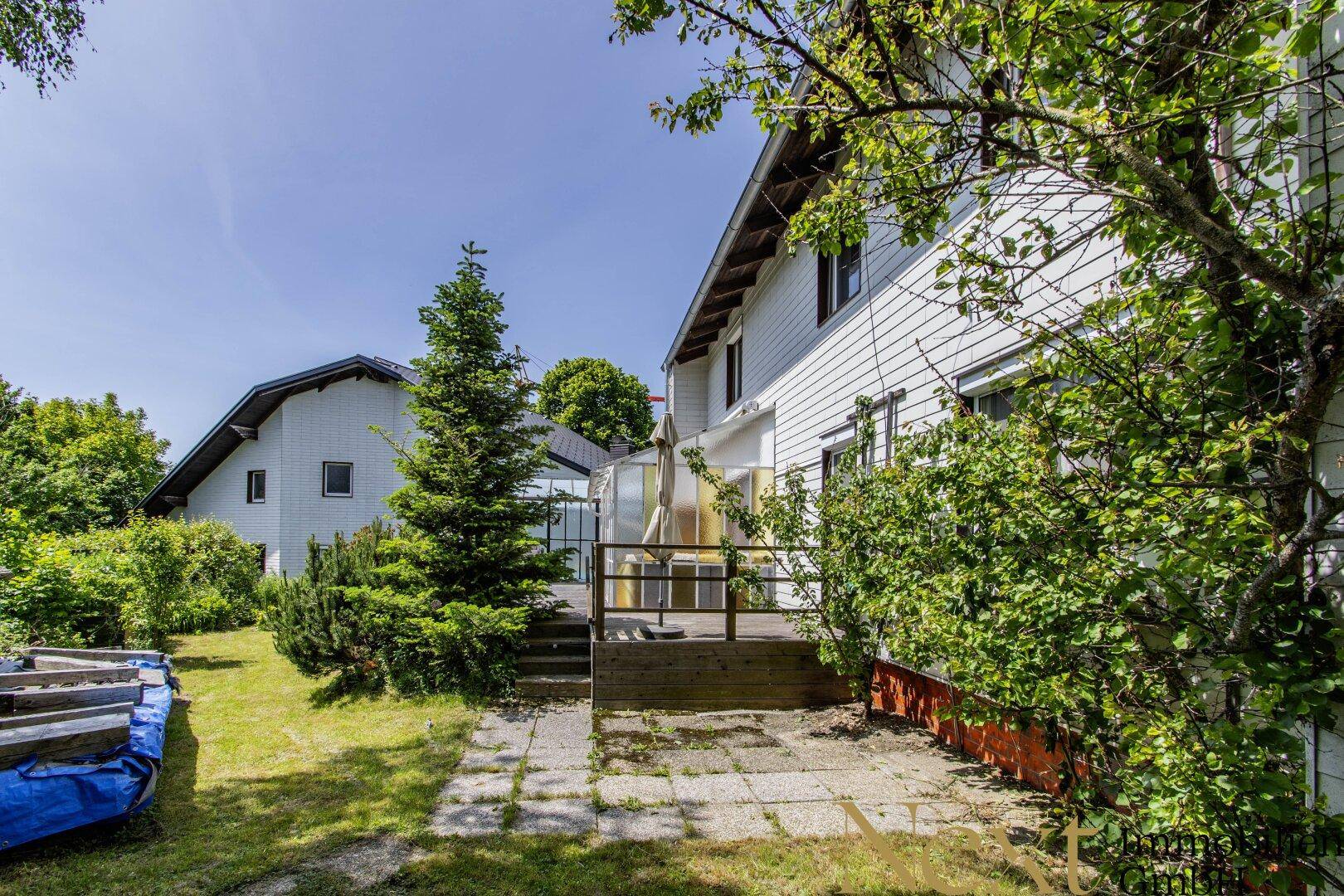 Gartenbereich mit Rasenfläche, Bäumen und einer Holzterrasse am Haus.