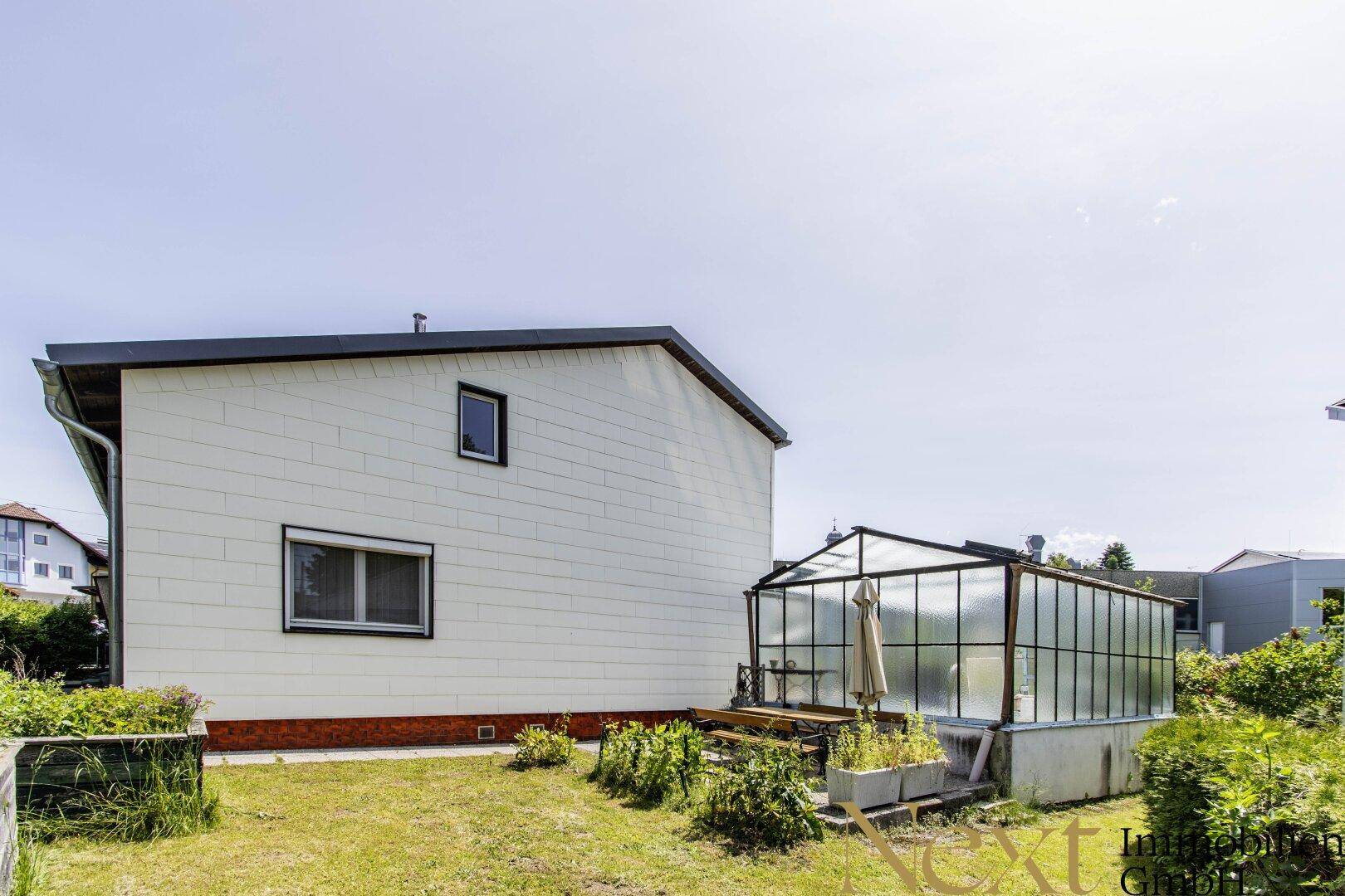 Garten mit Gewächshaus, Rasenfläche und Blick auf die Hausfassade.